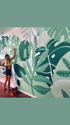 a woman painting a wall with green leaves on it