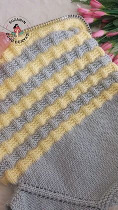 a hand is holding a gray and yellow knitted blanket