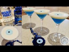 three glasses filled with blue liquid next to an evil eye keychain