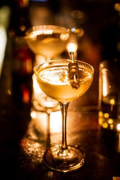 two martinis sitting on top of a table next to glasses filled with liquid and lit candles