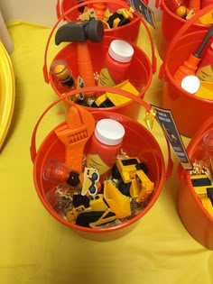 three buckets filled with construction toys on top of a yellow tablecloth covered table