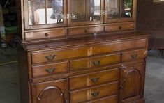 an old wooden china cabinet with glass doors and knobs on the front, sitting in a garage