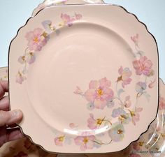 a person holding up a pink plate with flowers on the front and sides, in front of other plates