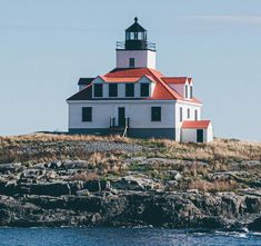 a white and red light house on top of a rocky hill next to the ocean