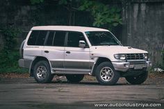 a white suv is parked in front of a concrete wall and some trees with green leaves