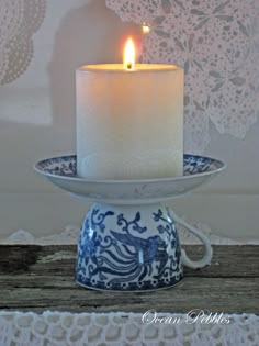 a lit candle sitting on top of a blue and white plate next to a lace doily