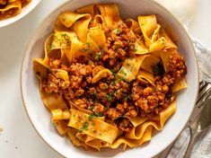 two bowls filled with pasta and meat on top of a white tablecloth next to utensils