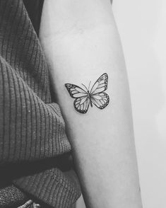 a black and white photo of a butterfly tattoo on the left inner arm, with an outline of a butterfly