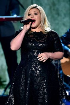 a woman in a black dress singing into a microphone