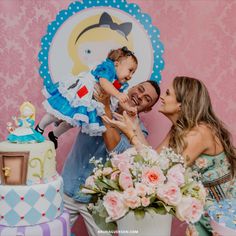 a man and woman holding a baby in front of a cake