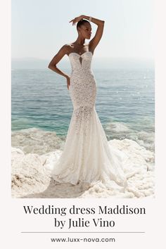 a woman in a wedding dress standing on the beach with her hands behind her head