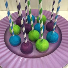 purple and green cake pops are on a plate with striped straws in the middle