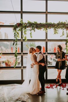 a bride and groom kiss as they stand in front of a window with rose petals on it