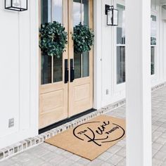 a welcome mat on the front door of a house with two wreaths hanging from it