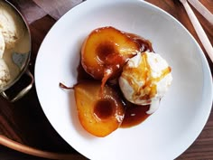 a white plate topped with ice cream and two pieces of fruit covered in caramel