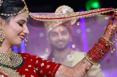 a woman in a red and gold bridal outfit holding up a piece of jewelry