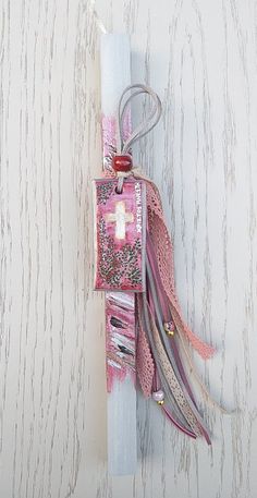 a white candle with pink and purple ribbons hanging from it's side on a wall