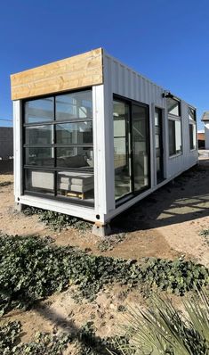 a small house made out of shipping containers on top of dry grass and dirt in the desert