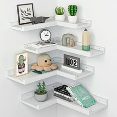 three white shelves with books, pictures and other items on them in the corner of a room