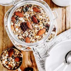 a glass jar filled with granola on top of a wooden table next to two spoons