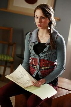 a young woman sitting on top of a wooden table holding a piece of paper in her hand