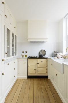 an old fashioned stove in a white kitchen with wood flooring and cupboards on both sides