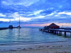 a pier on the beach with boats in the water and clouds above it at sunset