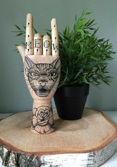 a wooden statue of a hand with the word meow painted on it next to a potted plant