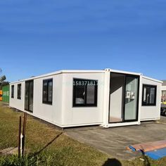 a white portable home sitting on top of a grass covered field next to a parking lot