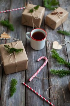 several wrapped presents and candy canes on a wooden table next to a cup of tea