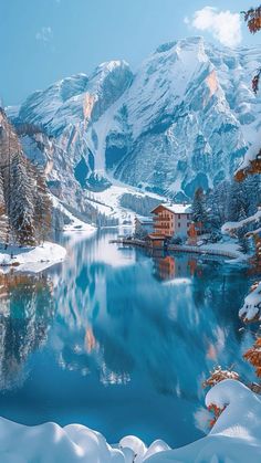 a lake surrounded by snow covered mountains with houses on the shore and trees in the foreground