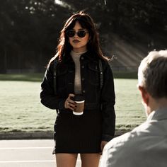 a woman standing in front of a man holding a coffee cup and talking to each other