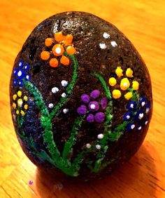 a painted rock sitting on top of a wooden table covered in lots of colorful flowers