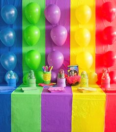 there are many balloons and cake on this rainbow colored table clothed with tissue paper