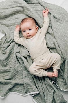 a baby laying on top of a bed under a blanket with his arms up in the air