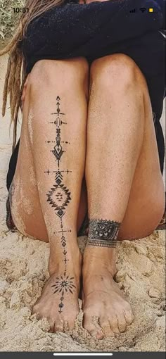 a woman sitting in the sand with her legs crossed and tattoos on her leg,