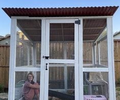 a woman standing in front of a small white chicken coop with doors open and windows on the side