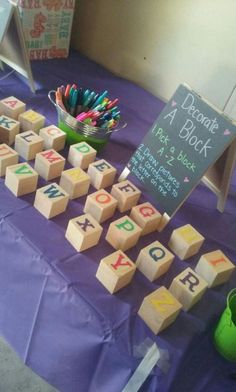 a purple table topped with wooden blocks covered in letters and numbers next to a green vase filled with colored pencils