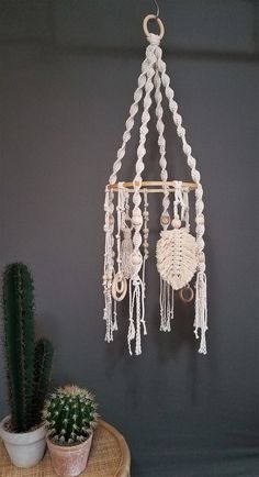 a white macrame dream catcher hanging on a wall next to a potted cactus