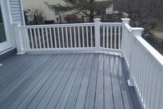 a wooden deck with white railings in front of a house