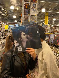 a woman holding up an album in front of her face while another person looks at it