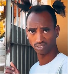 a man with black hair and piercings standing in front of a fence