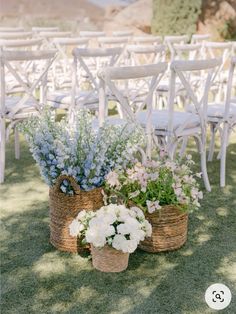 two baskets filled with flowers sitting on top of a grass covered field next to white chairs