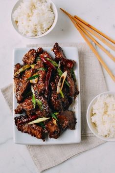 a white plate topped with meat next to rice and chopsticks on top of a table