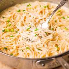 a pot filled with noodles and sauce on top of a wooden table next to a spoon