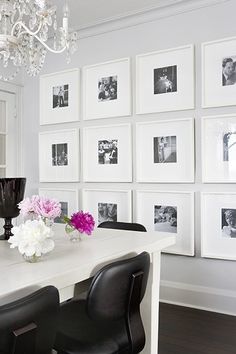 a white dining room table with black chairs and pictures on the wall behind it,