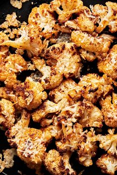 roasted cauliflower in a black pan on a stove top with seasoning sprinkles