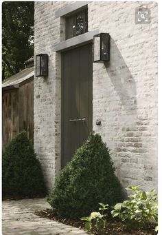 a white brick building with two green doors and some bushes in front of the door