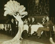 an old fashion photo of a woman with feathers on her head in front of people