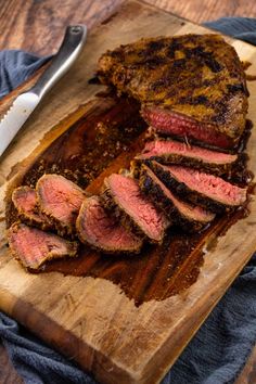 sliced meat sitting on top of a wooden cutting board next to a knife and fork